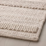 Close-up of handwoven, textured wool rug on light wood floor, showcasing intricate weave and natural fibers.