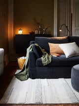 Cozy living room with dark blue BRÖNDEN rug, featuring various weaves and textures, placed under soft lighting.