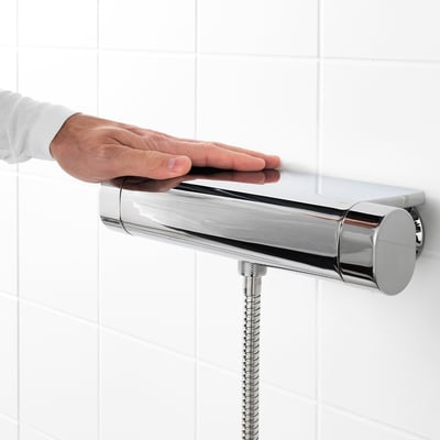 Person adjusting modern thermostatic shower mixer with safety stop feature.