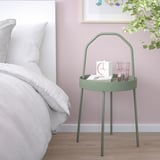 Green BURVIK side table with handle, clock, and glasses beside bed.