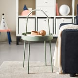Modern mint green side table with handle, round top, thin legs, tan accessories on top.