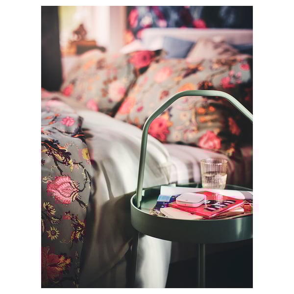Small green side table next to bed, holding books, remote, and glass.
