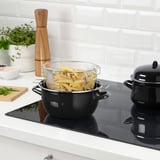 Fryer with mesh basket on black stove, white tiles in background.