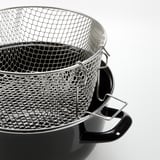 Stacked stainless steel frying baskets with black handles on a white surface.