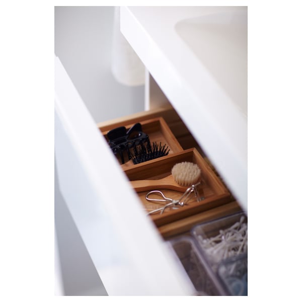 An open white drawer with a bamboo organizer holding hair clips, brush, and scissors.