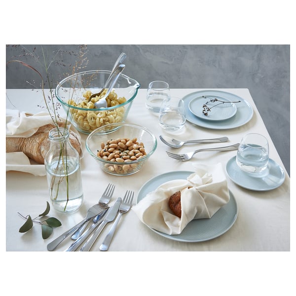 Table set with DRAGON silver cutlery on light blue plates, glasses, and bowls with food and flowers.
