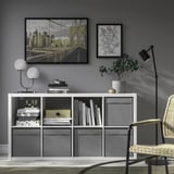 Modern living room with tv, storage unit, lamp, plant, artwork, and wicker chair.