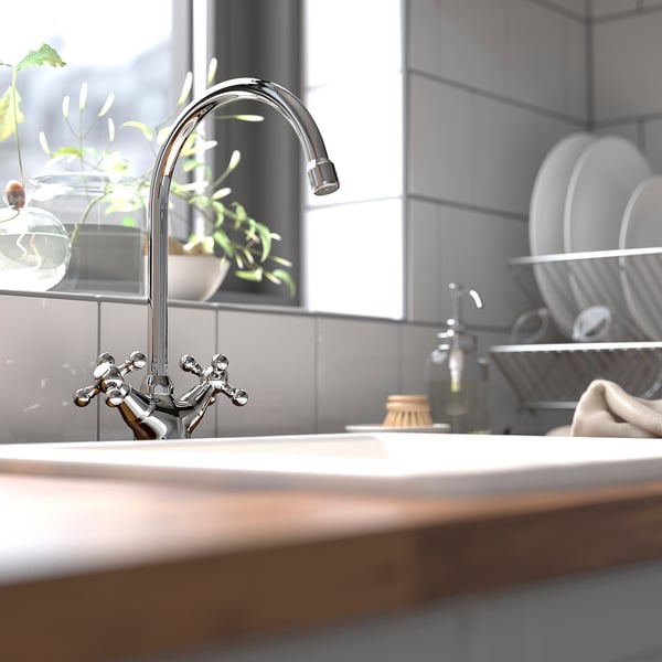 Chrome EDSVIK kitchen tap with high arc, plant, dish rack. Classic cross handles, white tiles, light countertop.