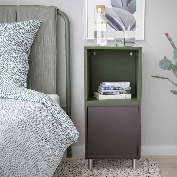 Bedside setup with green EKET shelf, books, succulent, picture frame, on patterned bedding, grey rug.