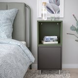 Bedside setup with green EKET shelf, books, succulent, picture frame, on patterned bedding, grey rug.
