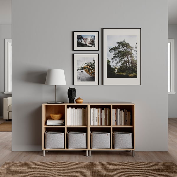 Modern living room with gray wall, large framed nature photos, and wooden bookcase.