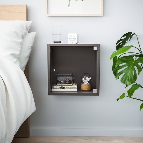 Bedside setup: EKET shelf, black, holds alarm, glass, typewriter, plant. Floating square shelf, modern style.