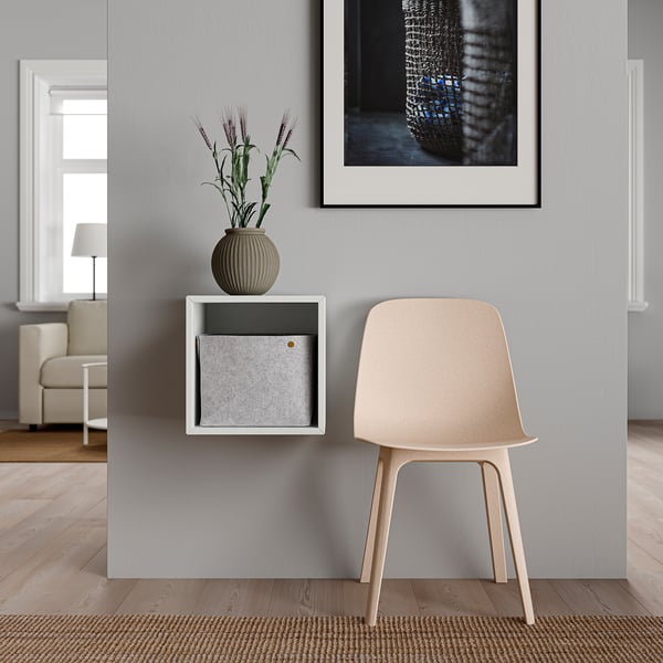 Minimalist chair & shelf combo: light-colored chair, wall-mounted white shelf with gray drawer, plant in beige vase, abstract art.