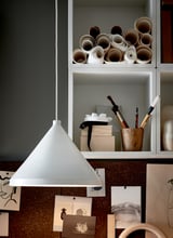 Modern white pendant lamp hangs near organized shelves with art supplies in white cabinet, blue wall.