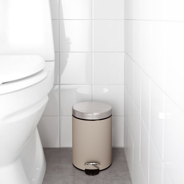 Beige bathroom trash can with foot pedal and handle, next to toilet.