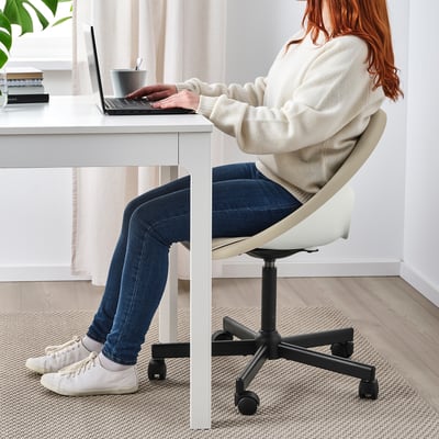 Person sitting on white ELDBERGET office chair, typing on laptop at white desk.