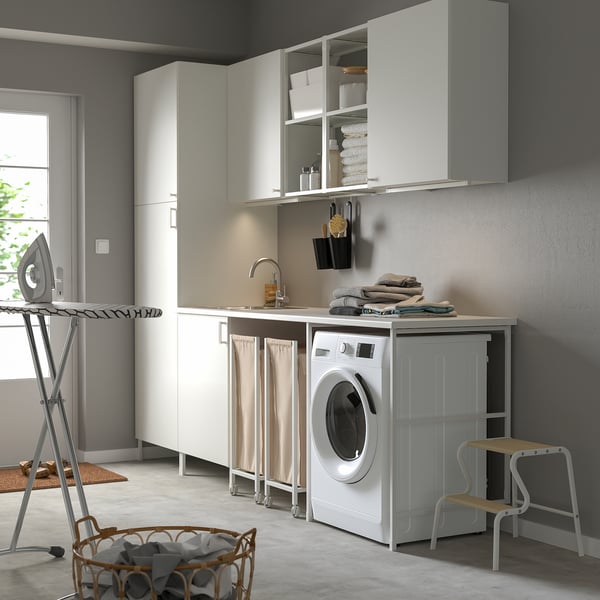 Modern laundry room with white ENHET cabinets. Washing machine, sink, and ironing board. Linen and cleaning supplies neatly stored.