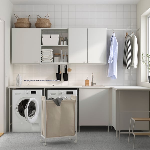 Modern laundry room with ENHET cabinets, washer, sink, hanging space, and laundry bag on wheels.