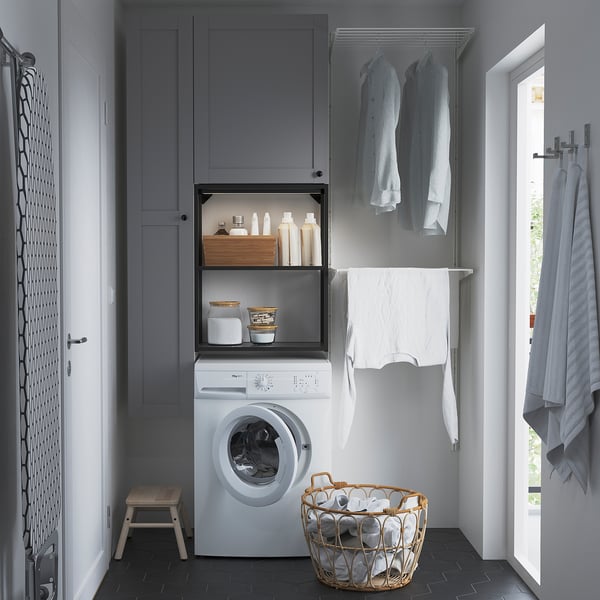 Modern grey ENHET laundry setup: washing machine, cabinets, and drying rack. Hangs clothes, stores detergent, and includes wicker basket.