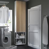 ENHET storage with doors & shelves holding laundry items & plant, beside ironing board.