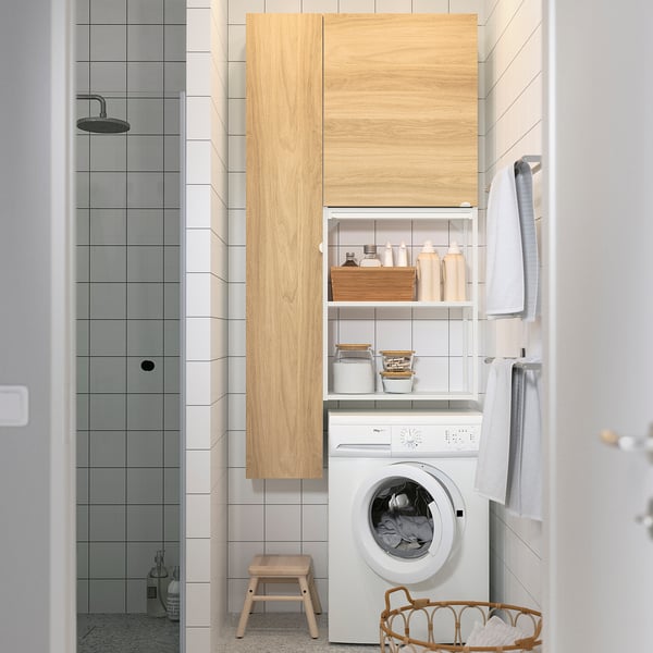 Modern bathroom with white tiled walls, a washing machine, and a wooden cabinet storing laundry items, creating a clean and organized space.