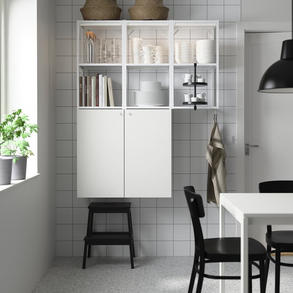 Modern kitchen with ENHET white cabinet & black stool, holding dishes & books, next to window with plant.