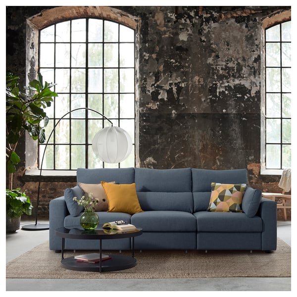 Modern living room with blue ESKILSTUNA sofa, colorful pillows, round coffee table, large arched windows, and floor lamp.