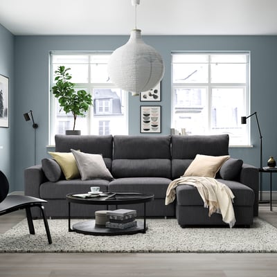 Modern living room with grey sectional sofa, adjustable headrests, and a pendant lamp above. Large window brings in natural light.