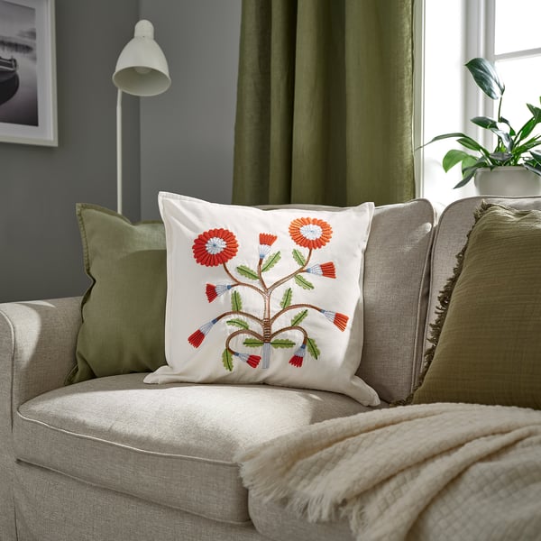 Decorative pillow named FACELIOR colorful florals on white cotton. Placed on a couch with curtains, its smaller than the cushions around it.
