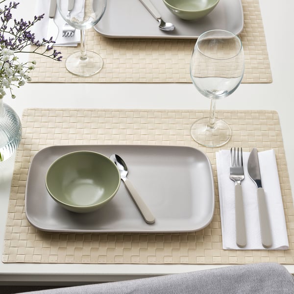 Table set with FÄRGKLAR plates, bowls, cutlery, and wine glasses on woven placemats.