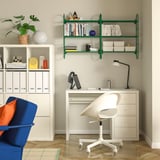 Modern home office with white desk, chair, green shelves, and blue seat.
