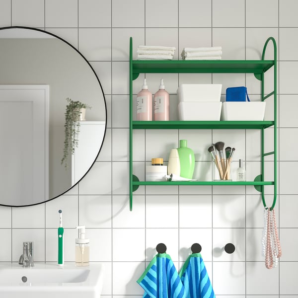 A modern bathroom with a large färgsätte wall shelf holding shampoo, towels, and makeup brushes, blue towels, and a round mirror beside it.