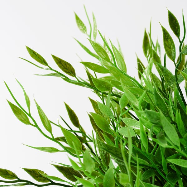 Bright green, lifelike leaves of an artificial plant, meticulously detailed with water droplets on each, arranged in a natural, bushy manner.