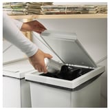 Person discarding a silver can into a white FILUR recycling bin with a lid.
