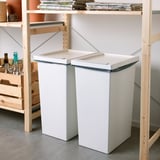 Two large white FILUR bins with lids sit between wooden shelves, holding bottles and magazines.