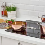 Modern kitchen with copper saucepan on induction hob, accompanied by ingredients and utensils.