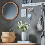 Wall mirror, woven basket, white vase with lilies, gray wall hooks, art prints.