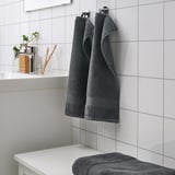 Dark gray fredriksjøn towels hang and fold neatly on white-tiled bathroom wall, contrasting with smaller items on the counter.
