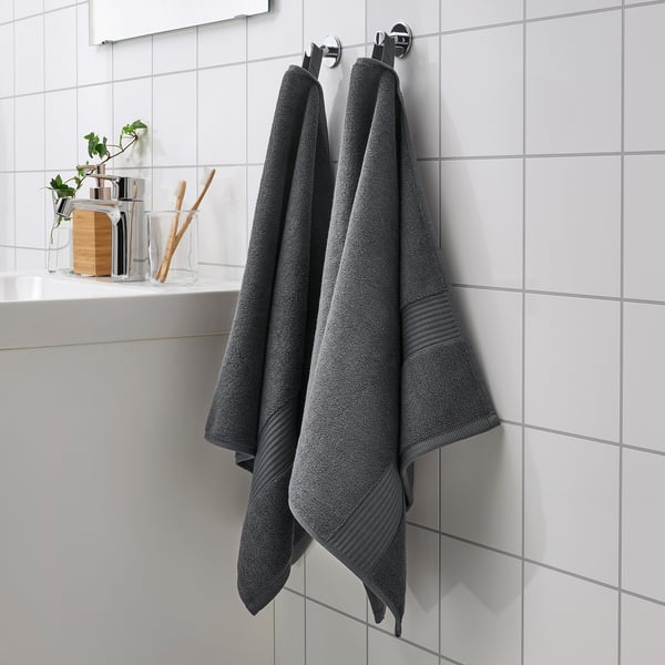 Two thick gray FREDRIKSJÖN towels hang on a hook next to a glass bathroom item holder.