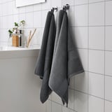 Two thick gray FREDRIKSJÖN towels hang on a hook next to a glass bathroom item holder.