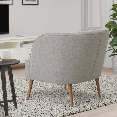 Modern grey barrel chair with wooden legs on speckled rug beside small table with white mug.
