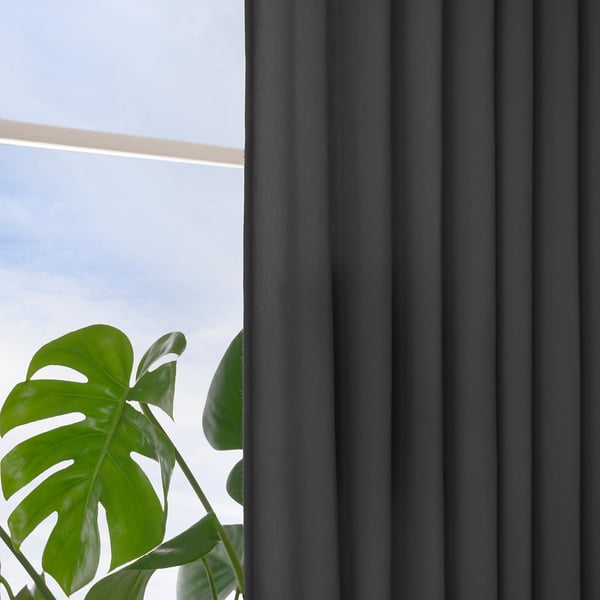 Dark grey curtains hang by window, offering privacy and light control. Large green leafy plant sits nearby.