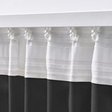 This image shows a close-up of white curtains with hooks, designed to hang on a curtain rod. The textured fabric allows light while providing privacy.