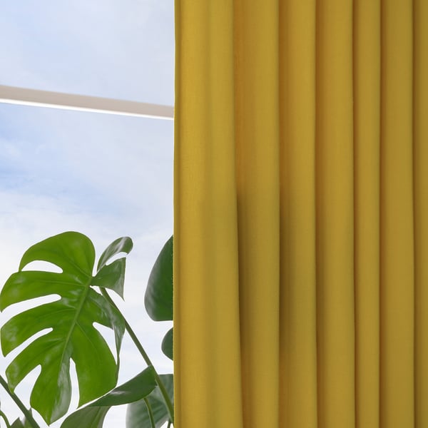 Bright yellow curtains hang by a window, letting in daylight while offering privacy. A green plant sits nearby, contrasting with the vibrant fabric.