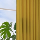 Bright yellow curtains hang by a window, letting in daylight while offering privacy. A green plant sits nearby, contrasting with the vibrant fabric.