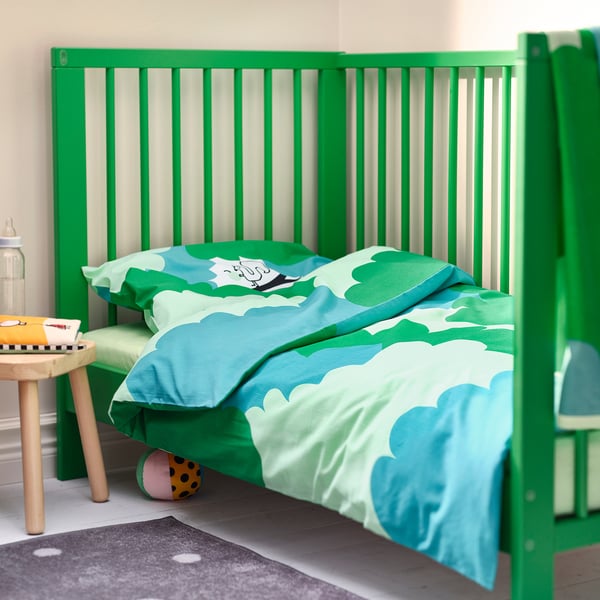 Bright green GRÖNFINK crib with blue, cloudy bedding. Smaller than adjacent wooden stool.