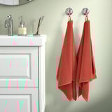 GULVIAL orange towels hang on modern bathroom hooks, white sink, chrome faucets, green wall - soft, fluffy, 100% cotton.