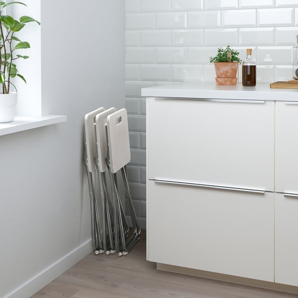Foldable white stools leaning against a kitchen cabinet. Space-saving design, ready for quick use.