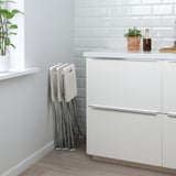 Foldable white stools leaning against a kitchen cabinet. Space-saving design, ready for quick use.