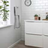 Modern kitchen with white cabinets, clock, plant, and wall-mounted towel heater.